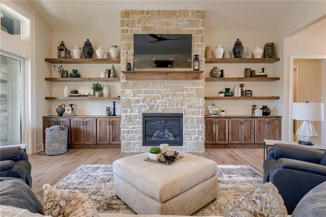 living room with a stone fireplace, vaulted ceiling, and light hardwood / wood-style flooring