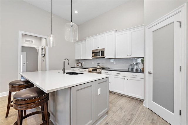 kitchen featuring pendant lighting, an island with sink, stainless steel appliances, sink, and light hardwood / wood-style flooring