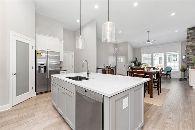 kitchen with appliances with stainless steel finishes, a center island with sink, sink, light hardwood / wood-style flooring, and hanging light fixtures