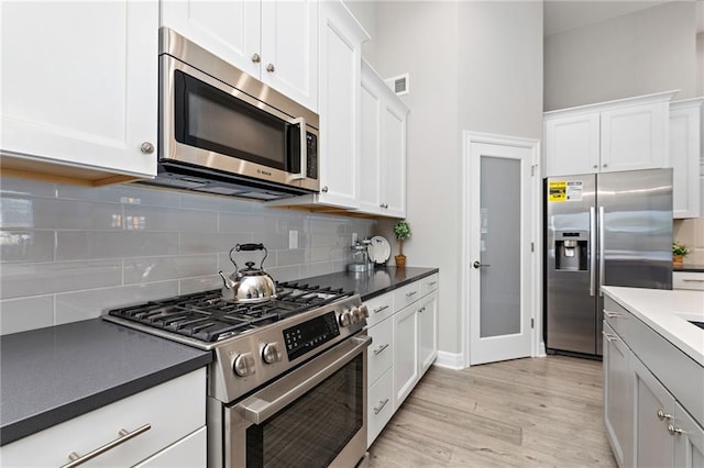 kitchen featuring high end appliances, tasteful backsplash, light hardwood / wood-style floors, and white cabinetry