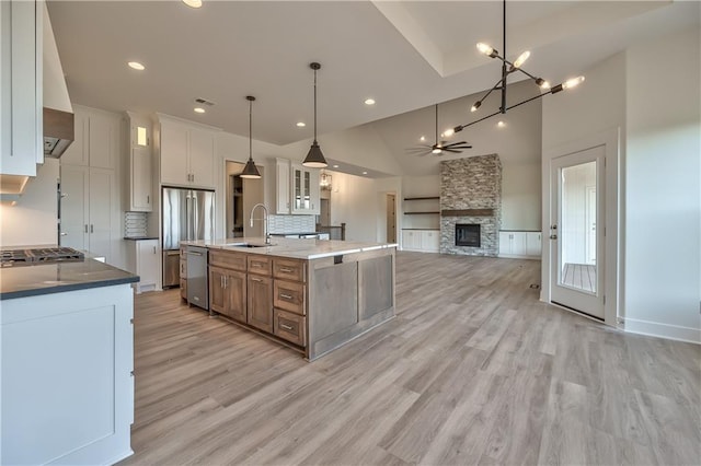 kitchen featuring sink, a stone fireplace, a kitchen island with sink, white cabinetry, and appliances with stainless steel finishes