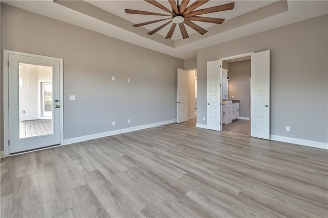 unfurnished bedroom with light wood-type flooring, connected bathroom, and a tray ceiling