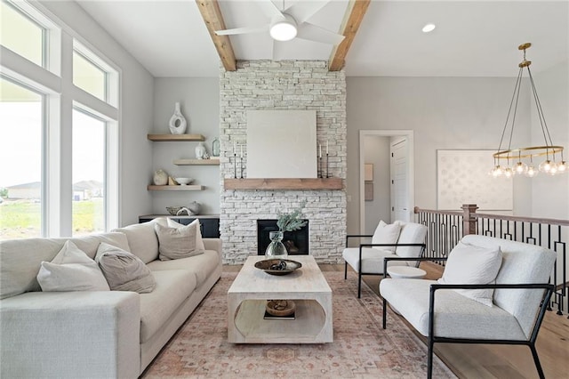 living room with ceiling fan with notable chandelier, a stone fireplace, light wood-type flooring, and a healthy amount of sunlight