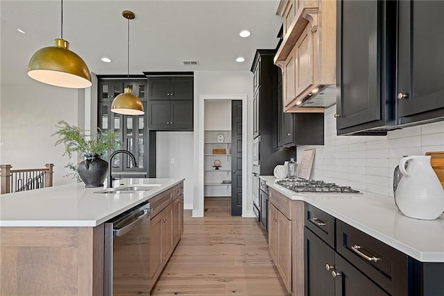 kitchen with pendant lighting, a kitchen island with sink, sink, light hardwood / wood-style flooring, and appliances with stainless steel finishes