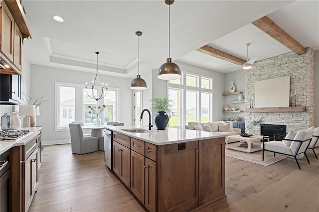 kitchen with an island with sink, sink, a stone fireplace, decorative light fixtures, and light hardwood / wood-style floors