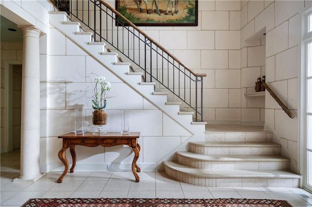 stairway featuring tile walls, light tile floors, and ornate columns