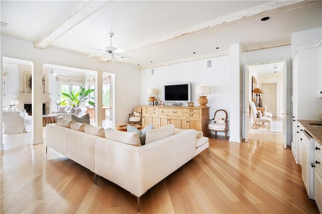 living room featuring ceiling fan, light hardwood / wood-style flooring, and beamed ceiling