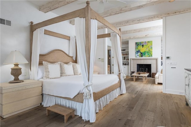 bedroom with beamed ceiling, ceiling fan, a tile fireplace, and light hardwood / wood-style flooring