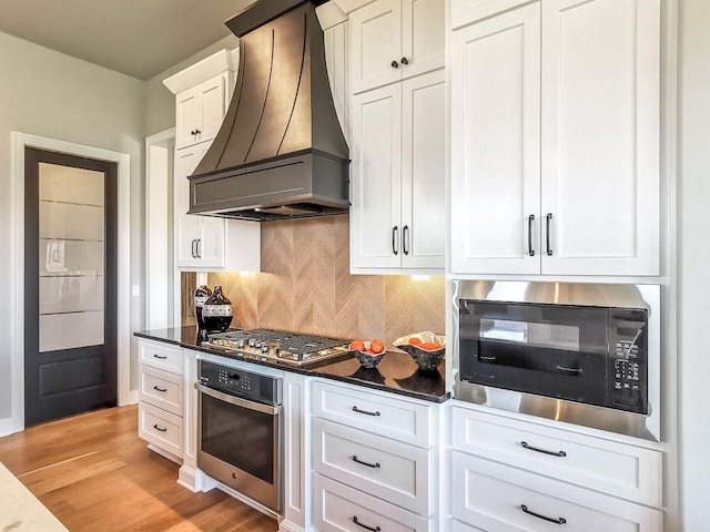2908 NE 102nd St, Kansas City, MO 64155 - kitchen featuring appliances with stainless steel finishes, custom range hood, light wood-type flooring, tasteful backsplash, and white cabinets
