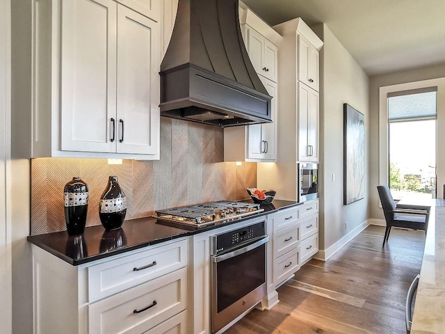 2908 NE 102nd St, Kansas City, MO 64155 - kitchen featuring backsplash, dark wood-type flooring, stainless steel appliances, premium range hood, and white cabinets