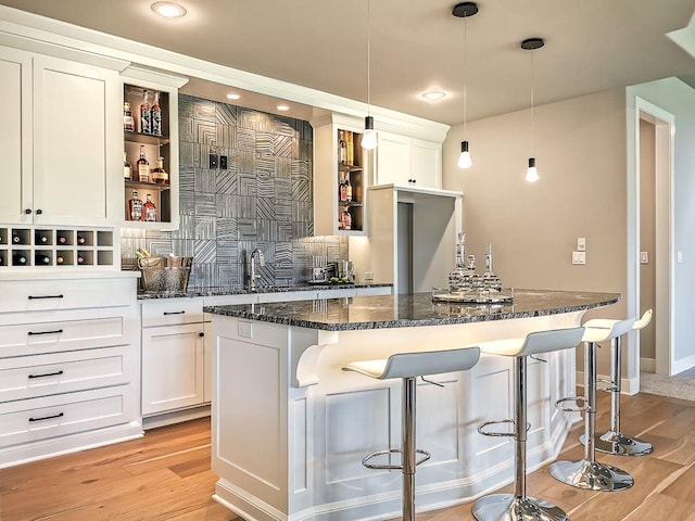 2908 NE 102nd St, Kansas City, MO 64155 - kitchen with hanging light fixtures, dark stone counters, light wood-type flooring, a breakfast bar area, and white cabinetry