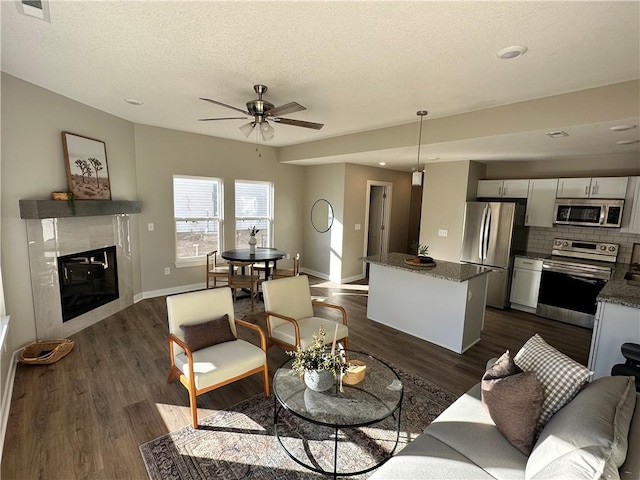 living room featuring a textured ceiling, a tile fireplace, ceiling fan, and dark hardwood / wood-style floors