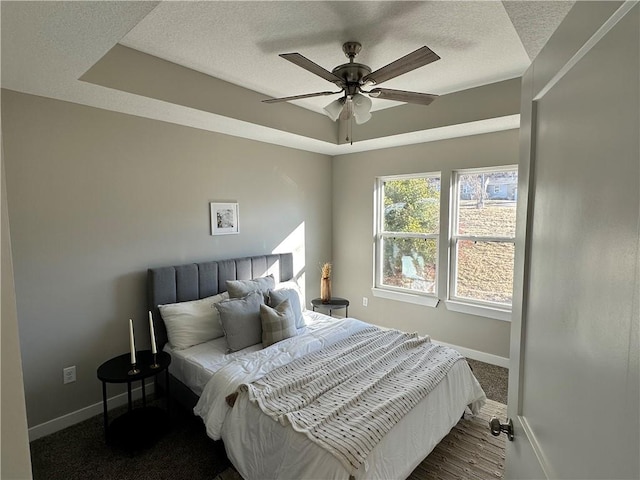 bedroom featuring ceiling fan, dark colored carpet, a raised ceiling, and a textured ceiling