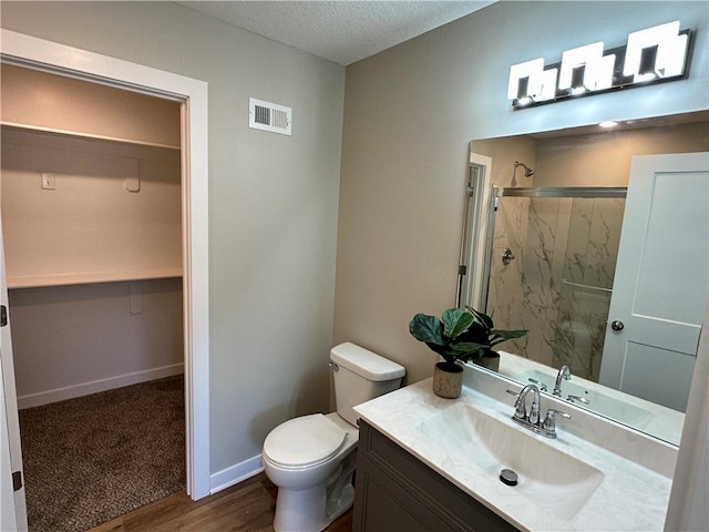 bathroom with toilet, a shower with door, a textured ceiling, vanity, and hardwood / wood-style flooring