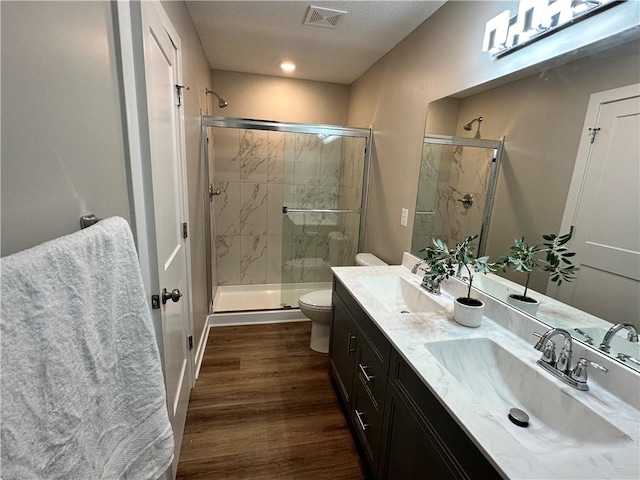 bathroom featuring toilet, hardwood / wood-style flooring, a shower with door, vanity with extensive cabinet space, and dual sinks