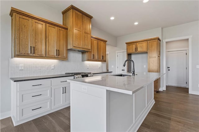 11606 S Zarda Dr, Olathe, KS 66061 - kitchen featuring tasteful backsplash, an island with sink, brown cabinetry, a sink, and dark wood-type flooring