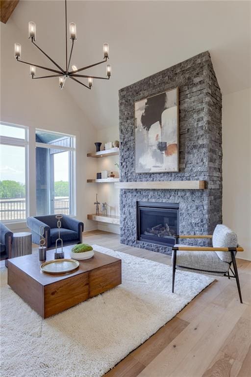 living room with light wood-type flooring, high vaulted ceiling, a chandelier, and a stone fireplace