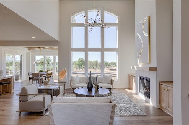 living room with a notable chandelier, a tile fireplace, light hardwood / wood-style flooring, and a towering ceiling