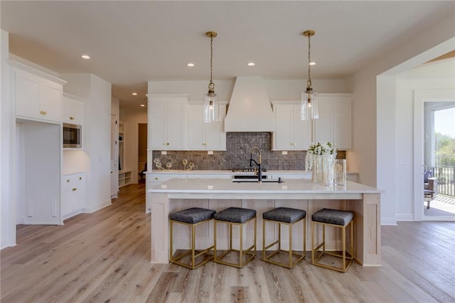 kitchen featuring hanging light fixtures, a kitchen island with sink, a kitchen breakfast bar, light wood-type flooring, and white cabinets