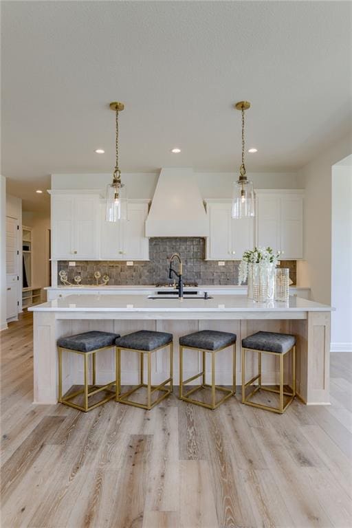 kitchen with white cabinets, hanging light fixtures, a center island with sink, and a breakfast bar area