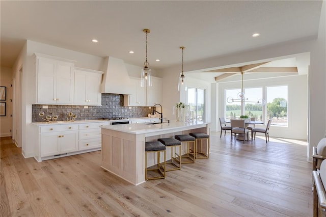 kitchen featuring light hardwood / wood-style flooring, a kitchen island with sink, white cabinets, and custom exhaust hood