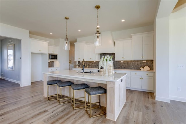 kitchen featuring white cabinets, premium range hood, and a kitchen island with sink