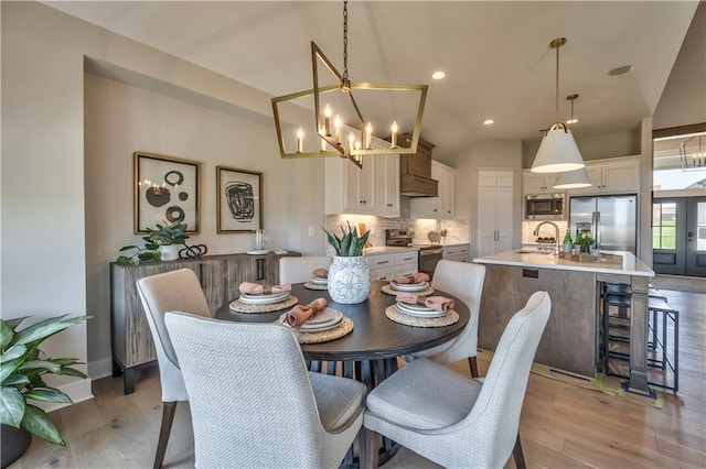 dining area featuring lofted ceiling, a chandelier, sink, and light wood-type flooring