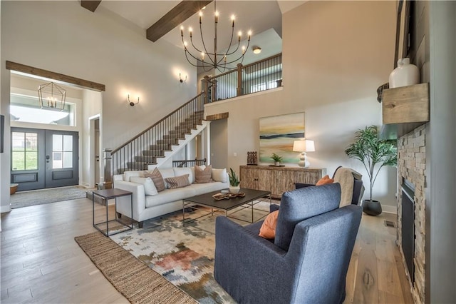 living room with a notable chandelier, a high ceiling, light wood-type flooring, and french doors