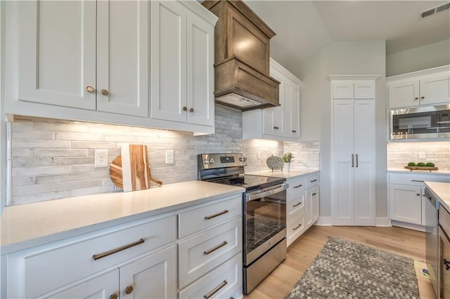 kitchen with appliances with stainless steel finishes, backsplash, light wood-type flooring, and white cabinets