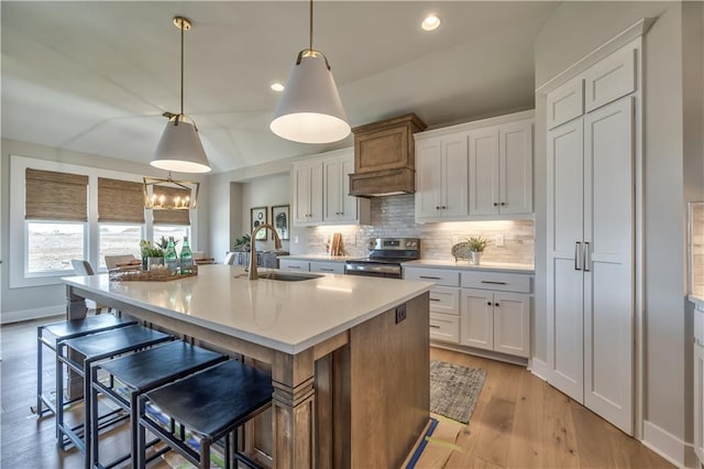 kitchen with hanging light fixtures, premium range hood, sink, white cabinetry, and electric range