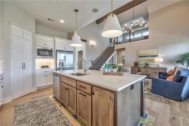 kitchen featuring an island with sink, hanging light fixtures, white cabinets, stainless steel appliances, and light wood-type flooring