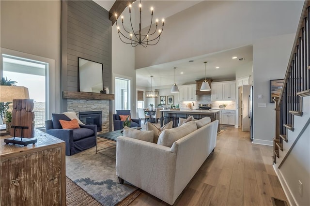 living room featuring a notable chandelier, light wood-type flooring, a high ceiling, and a stone fireplace