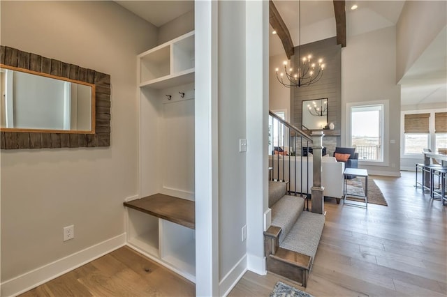 mudroom featuring beam ceiling, a notable chandelier, light wood-type flooring, and a towering ceiling