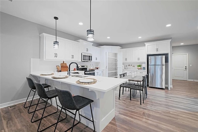 kitchen featuring white cabinetry, appliances with stainless steel finishes, hardwood / wood-style floors, decorative light fixtures, and sink