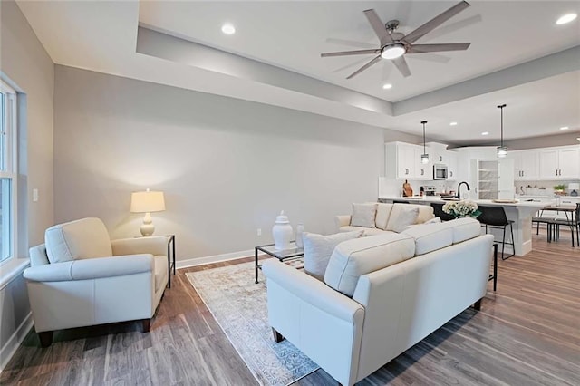 living room featuring hardwood / wood-style floors, sink, ceiling fan, and a raised ceiling