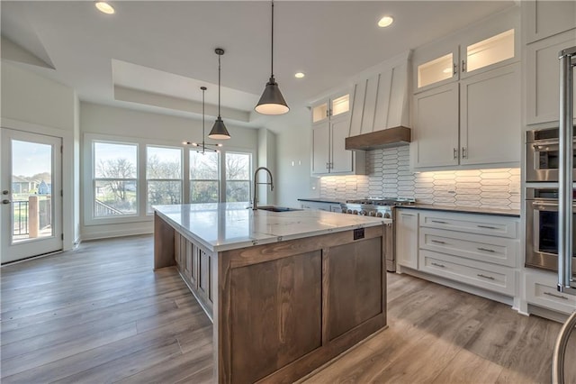 kitchen featuring appliances with stainless steel finishes, a center island with sink, white cabinetry, and pendant lighting