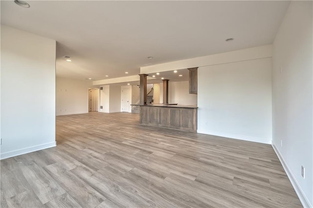 unfurnished living room with decorative columns and light hardwood / wood-style floors