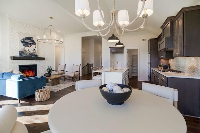 dining room featuring vaulted ceiling, a notable chandelier, sink, a stone fireplace, and dark hardwood / wood-style floors