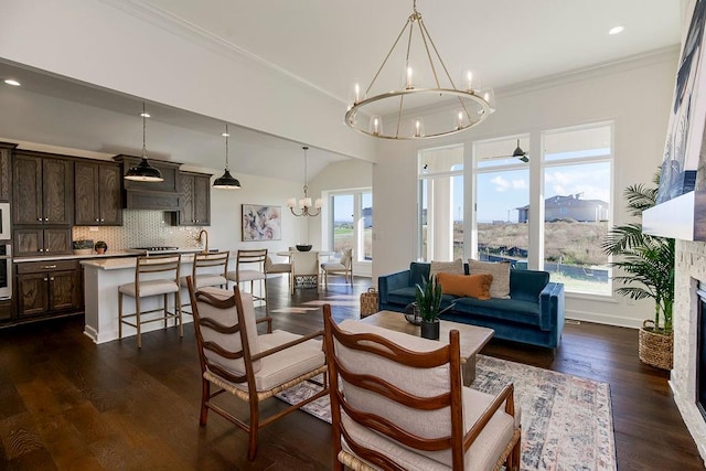 living room featuring lofted ceiling, a stone fireplace, a notable chandelier, crown molding, and dark hardwood / wood-style flooring