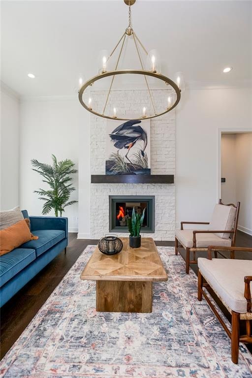 living room featuring an inviting chandelier, ornamental molding, dark hardwood / wood-style flooring, and a stone fireplace