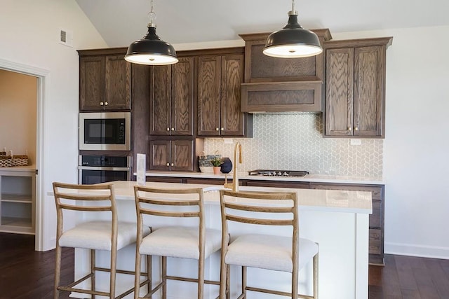 kitchen featuring dark brown cabinetry, an island with sink, dark wood-type flooring, stainless steel appliances, and vaulted ceiling