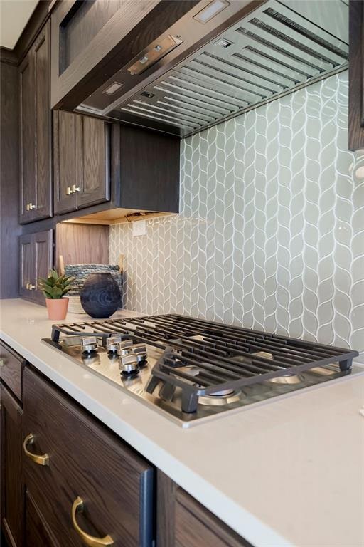 kitchen with dark brown cabinets, premium range hood, tasteful backsplash, and stainless steel gas cooktop