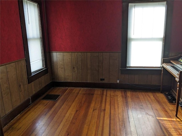 empty room featuring dark hardwood / wood-style floors, wooden walls, and plenty of natural light