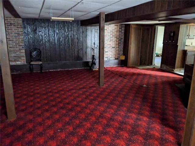 basement with brick wall, dark colored carpet, and a drop ceiling