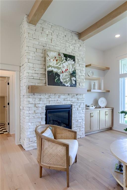 sitting room with beamed ceiling, light wood-type flooring, and a stone fireplace