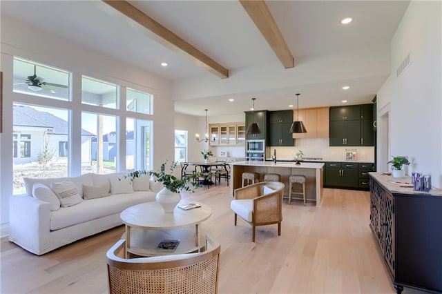 living room featuring a high ceiling, ceiling fan with notable chandelier, sink, beam ceiling, and light hardwood / wood-style floors