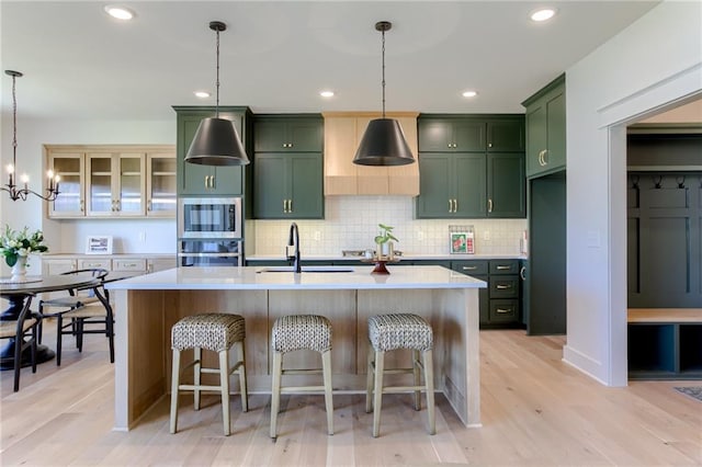 kitchen featuring pendant lighting, stainless steel appliances, light hardwood / wood-style flooring, and an island with sink