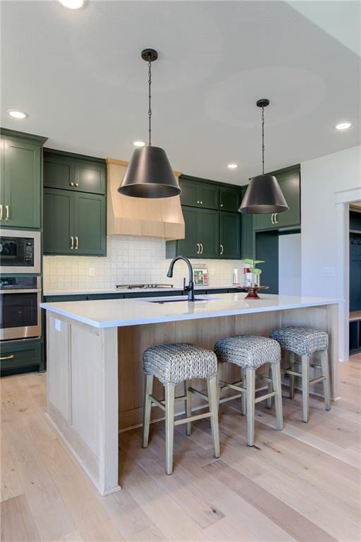 kitchen featuring green cabinets, stainless steel oven, light hardwood / wood-style floors, and a center island with sink