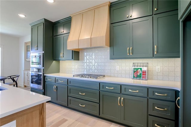 kitchen with premium range hood, green cabinetry, light hardwood / wood-style flooring, tasteful backsplash, and stainless steel gas cooktop