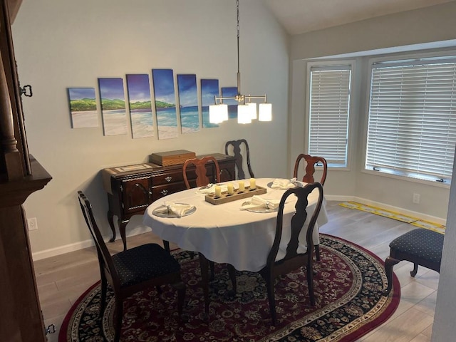 dining area with a chandelier, light wood-type flooring, and vaulted ceiling